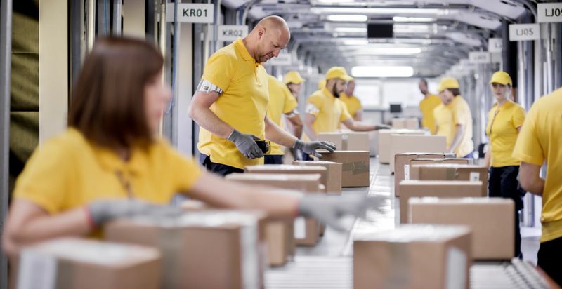 Workers processing boxes on conveyor belt in distribution warehouse.