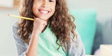 Smiling girl holding pencil, ready to write or draw.
