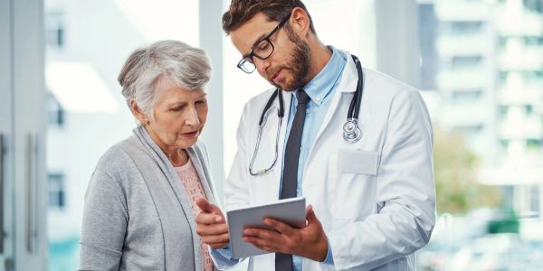 Doctor consulting elderly woman using digital tablet.