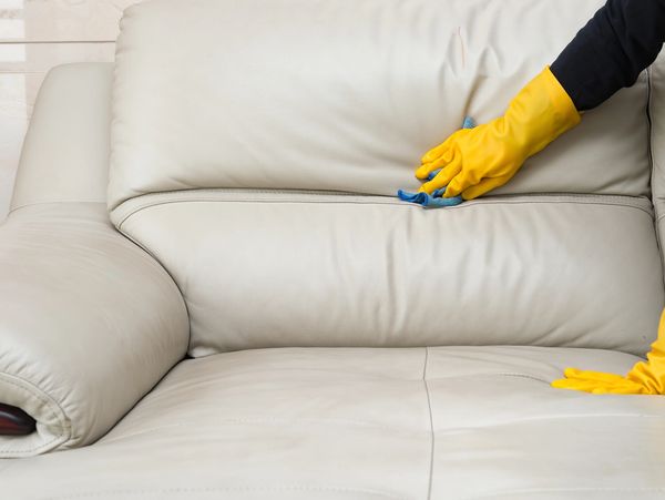 Person cleaning a white leather sofa with yellow gloves.