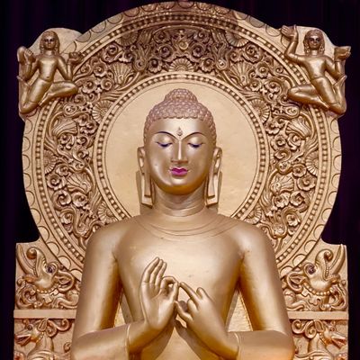 Golden Buddha statue with intricate backdrop and serene expression.