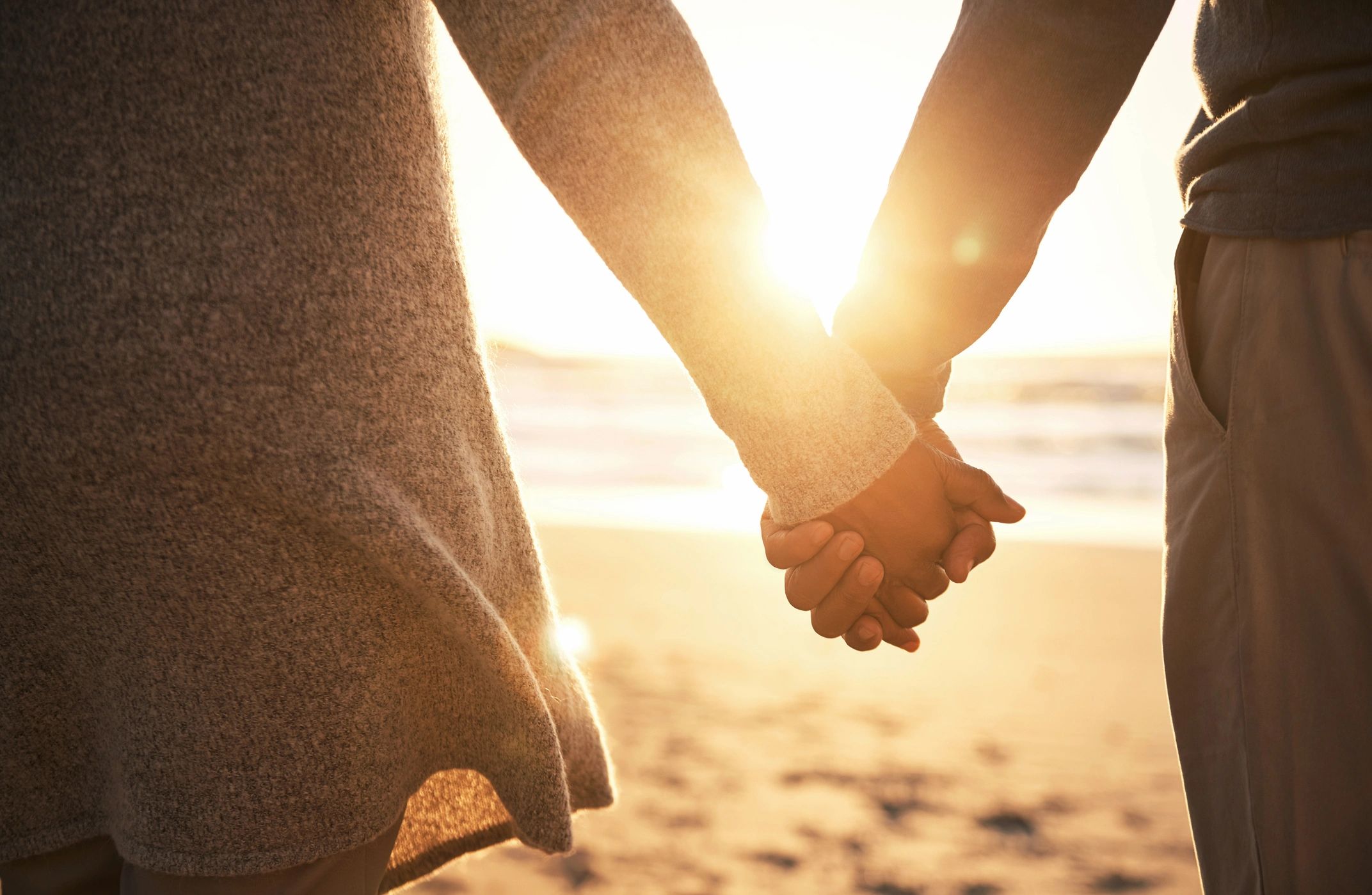 Couple holding hands with the sun in the background.
