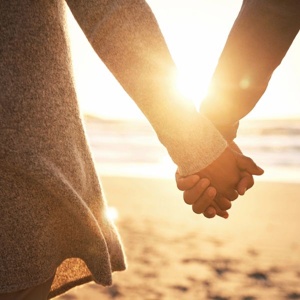 Two people holding hands at the beach during sunset.