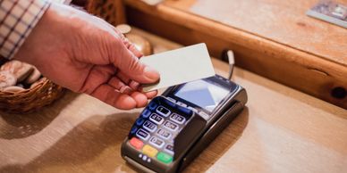 Hand holding a card near a card payment terminal for contactless payment.