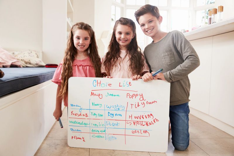 Portrait Of Children Making List Of Chores On Whiteboard At Home