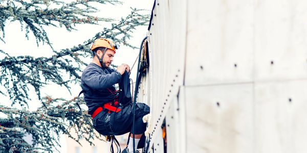 A worker wearing safety gear rappelling down a building.