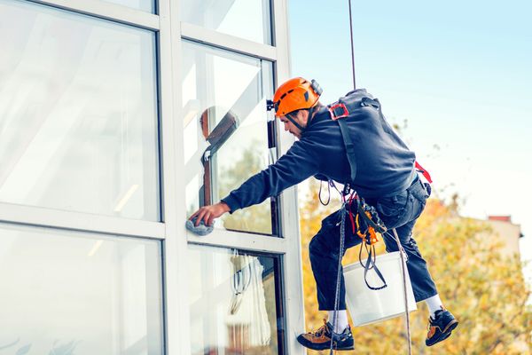A professional window cleaner suspended by ropes cleans a high-rise building's exterior windows.