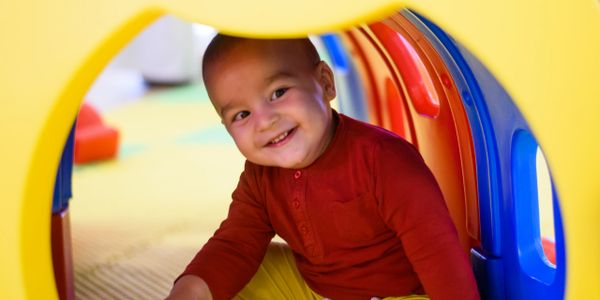 Smiling toddler playing inside colorful plastic tunnel.