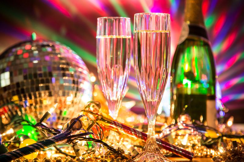 New Year's Eve celebration party with champagne, glasses, disco ball, decorations including beads, lights, blow horns and confetti.
