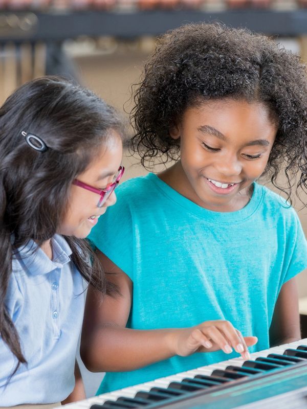 Two girls happily playing a piano together.
