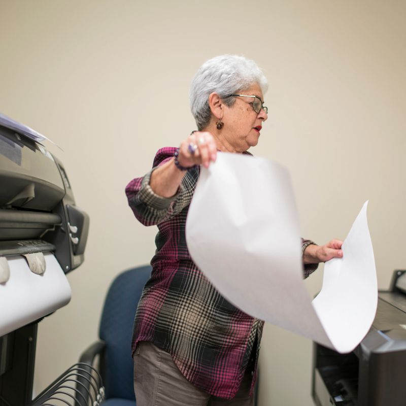 Senior silver-haired woman, engeneer, using the commercial wide format printer in the office.