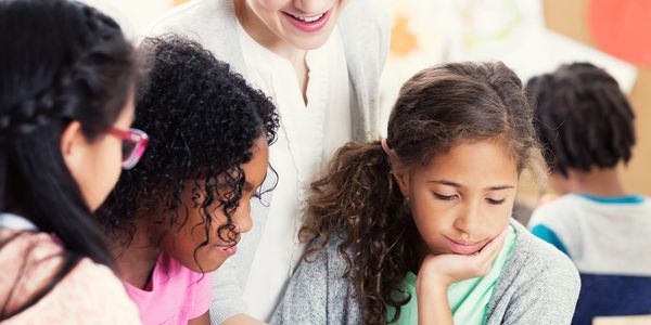 Teacher helping young students learn from a book in a classroom.
