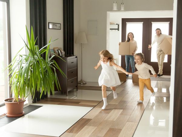 Happy kids running inside a new home while parents carry moving boxes.