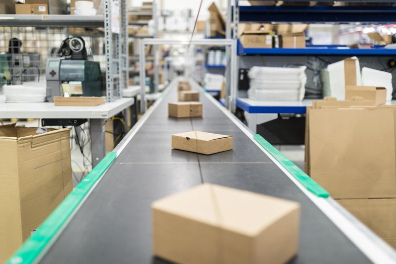 Cardboard boxes on moving belt conveyor at distribution warehouse. Modern warehouse with automatic moving conveyor machine.