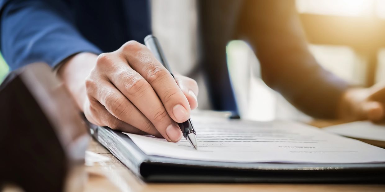 A person signing a document with a pen on a clipboard.