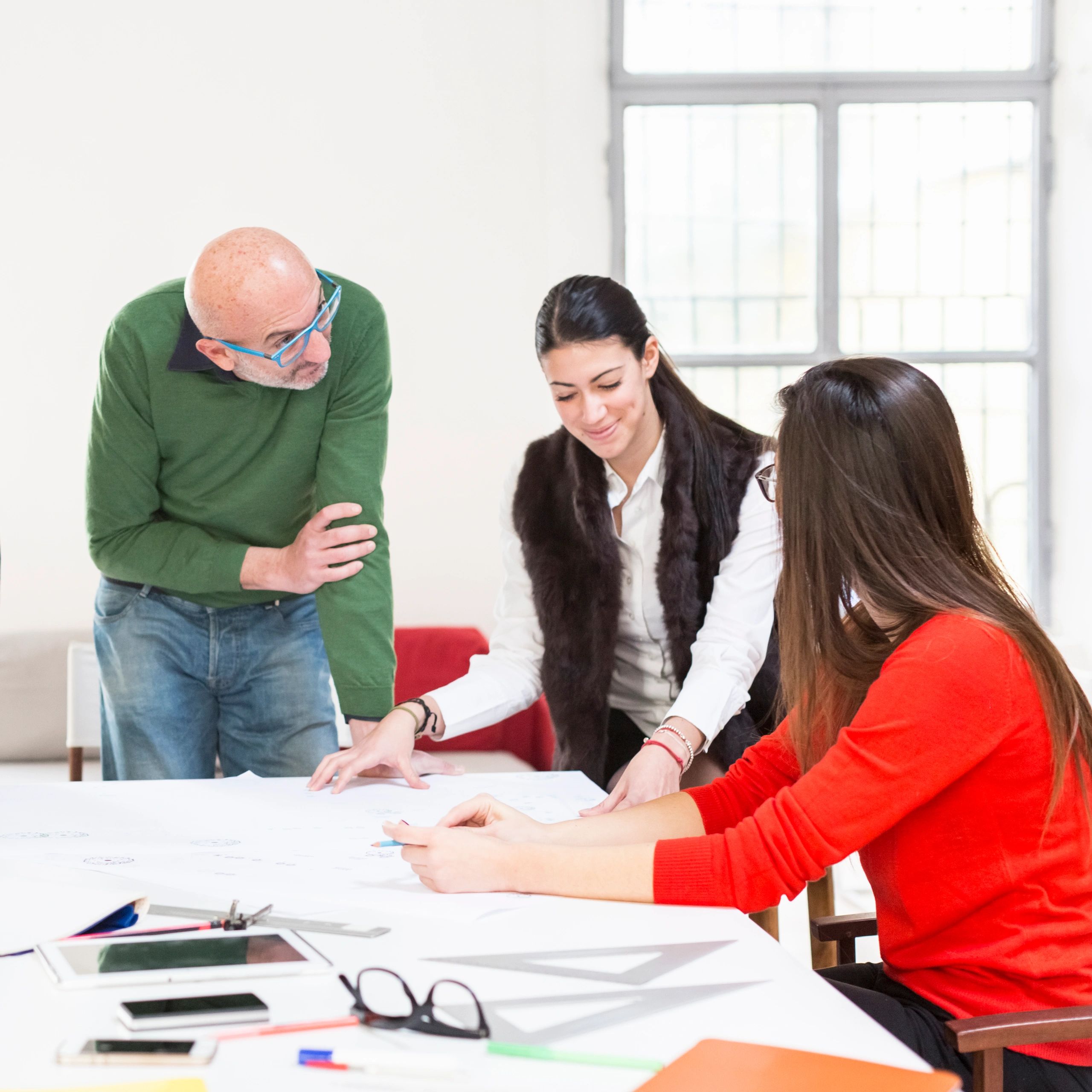 Three colleagues collaborating over a large blueprint in a bright office.