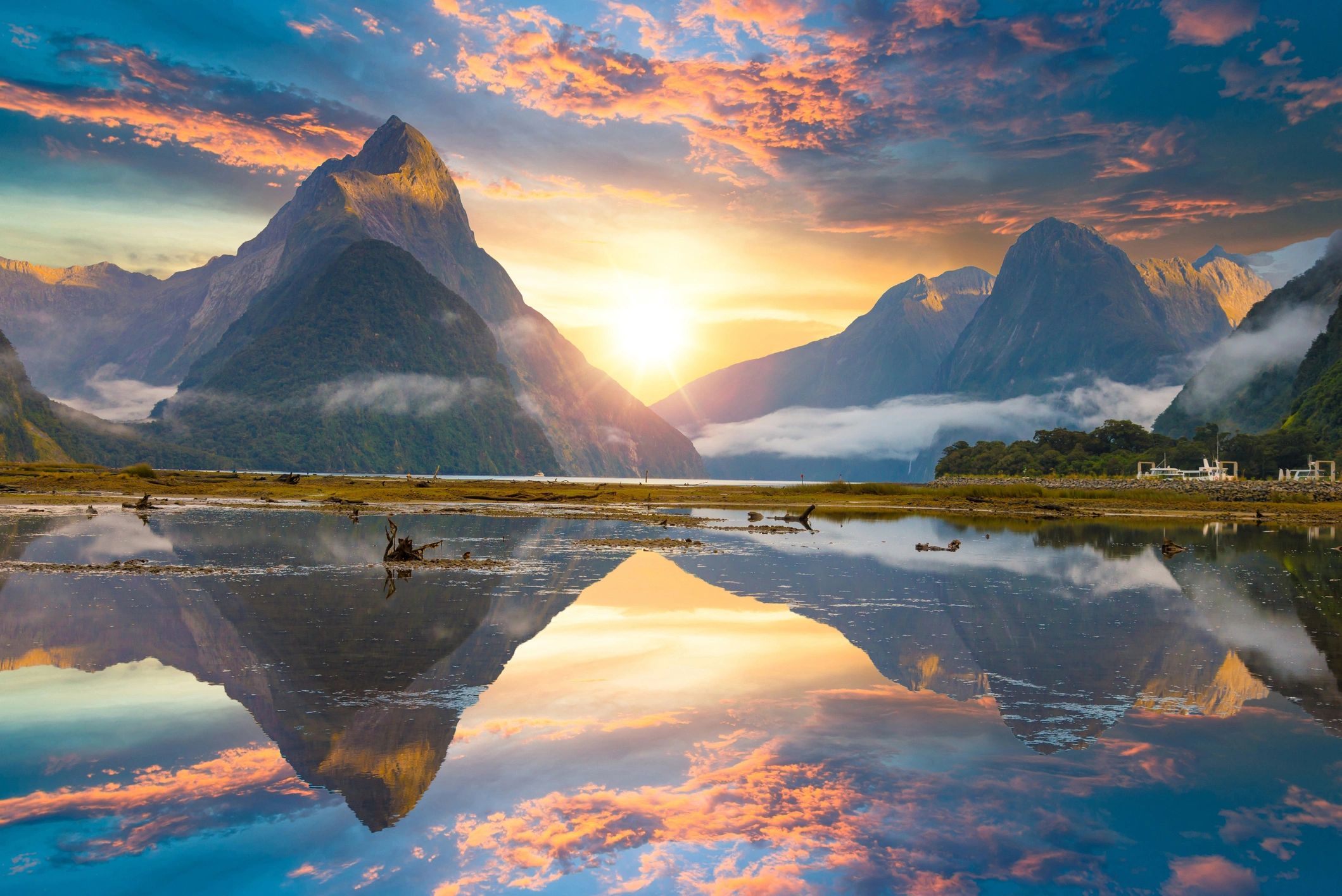 Sunset over misty mountains with reflection in calm water.