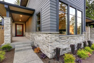 Modern house exterior with stone and wood siding, large windows, and landscaped entrance.