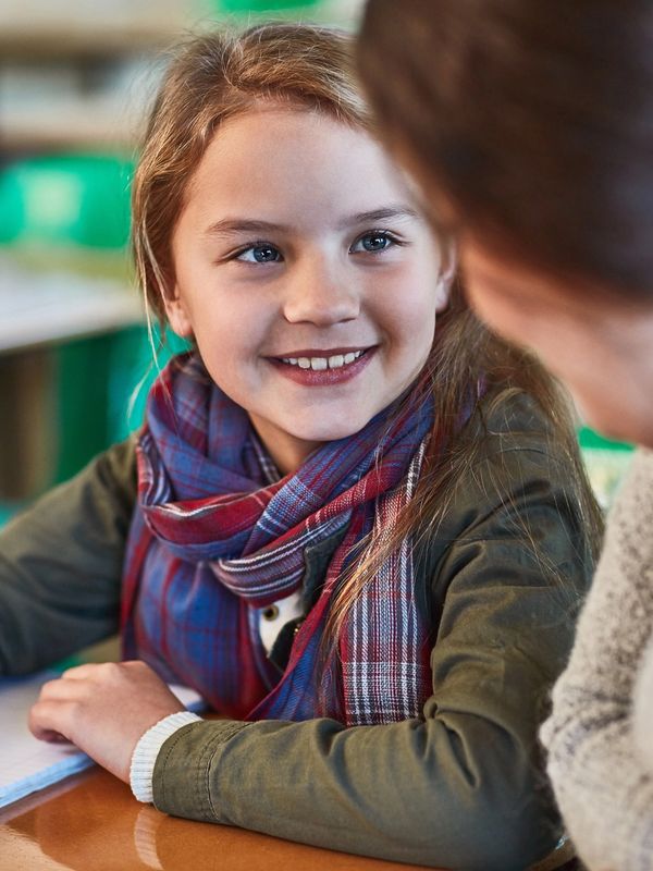 Young student smiling while writing in a notebook during a classroom interaction.