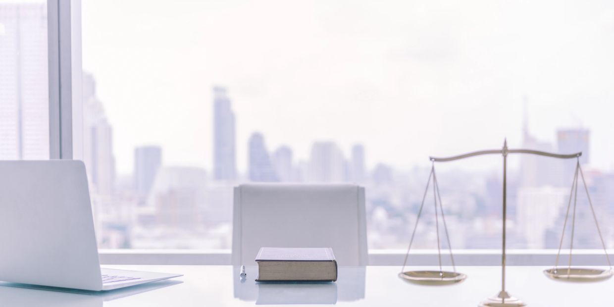Modern law office desk with laptop, book, pen, and scales of justice.