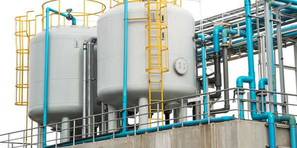 Industrial water tanks with blue pipes and yellow ladders on a concrete platform.