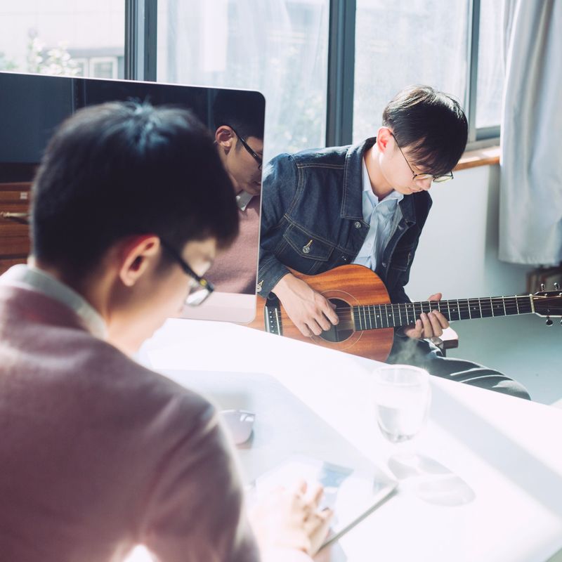 young man playing guitar while his friend sitting by computer.