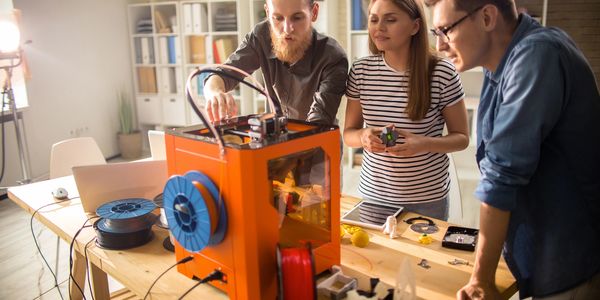 Three people working together on a 3D printing project in a bright office.