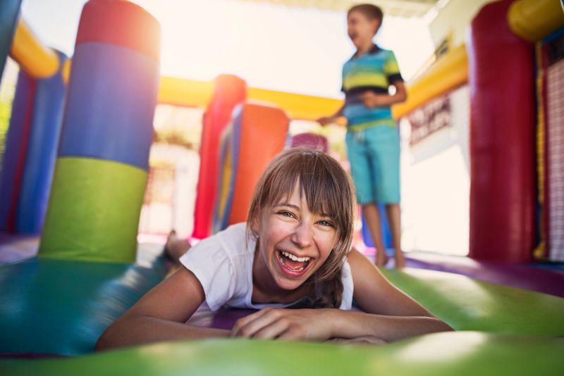 Boy and girl having fun jumping in inflatable castle playground. Sunny summer day
