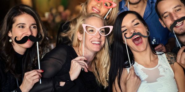 Group of friends having fun with fake mustaches and glasses at a party.