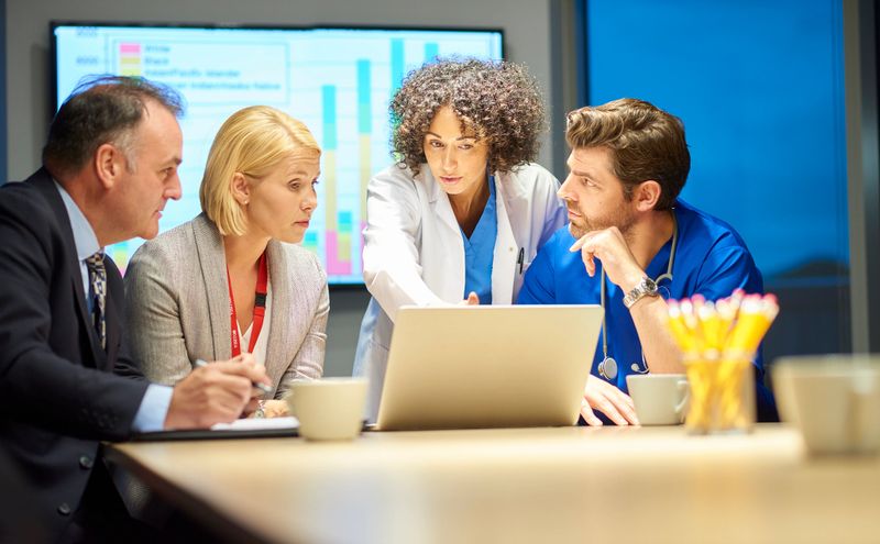 a mixed group of healthcare professional and business people meet around a conference table .