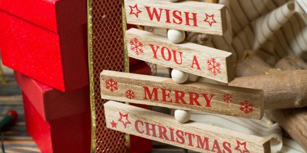 Wooden Christmas sign with red text next to gifts.