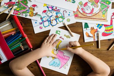 Child coloring holiday-themed drawings at a wooden table.