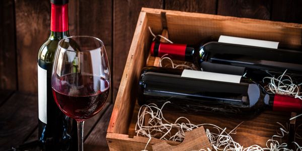 A glass of red wine beside a wooden crate with red wine bottles.