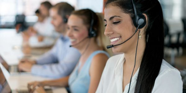 Customer service representatives wearing headsets and smiling while working.
