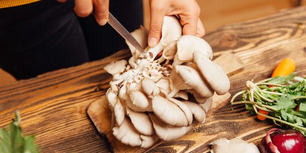 Person cutting oyster mushrooms on a wooden board.