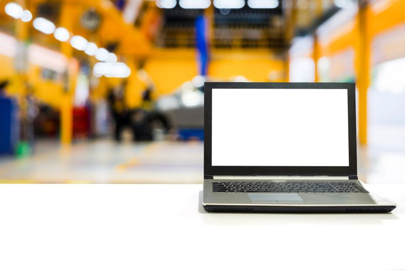 Laptop on white desk with blurred scene car garage with maintenance and fixing