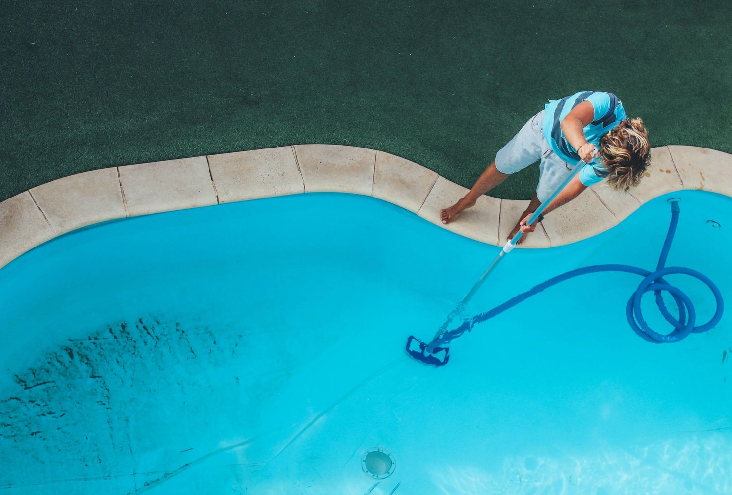Person cleaning a swimming pool with a vacuum.