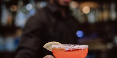 Person holding a colorful cocktail with a salted rim.