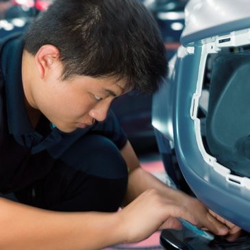 Man inspecting or fixing a part of a vehicle's rear bumper.