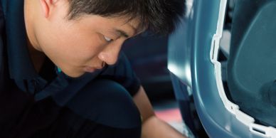 A man closely inspects and cleans a car's front bumper area.
