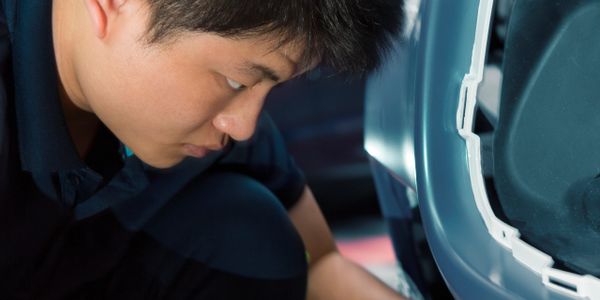 A man closely inspecting a car's undercarriage or tire area.