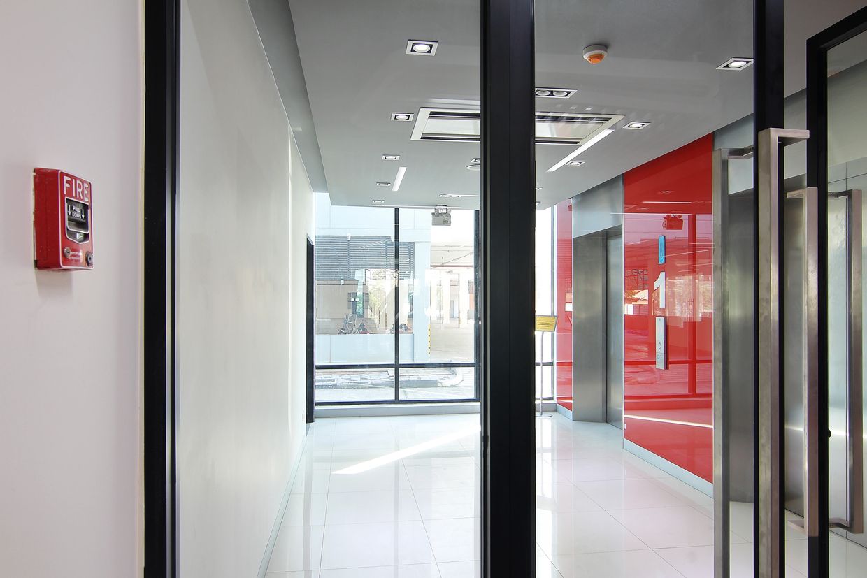 Modern elevator lobby with red accent wall and glass doors.