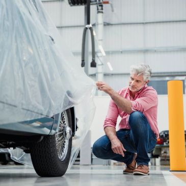 Man inspecting a covered car in a garage.