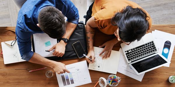 Four people collaborating over charts, notes, and laptops at a wooden table.