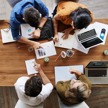 Four people collaborate at a wooden table with laptops, graphs, and notes.
