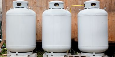 Three large propane tanks standing on concrete blocks outdoors.