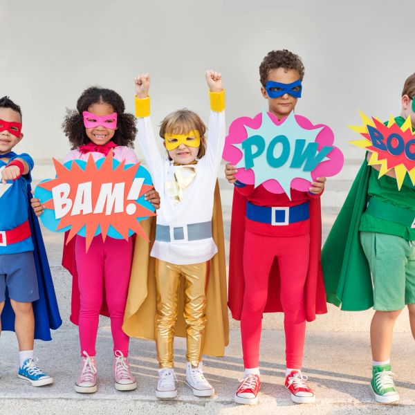 Kids dressed as superheroes holding comic signs.