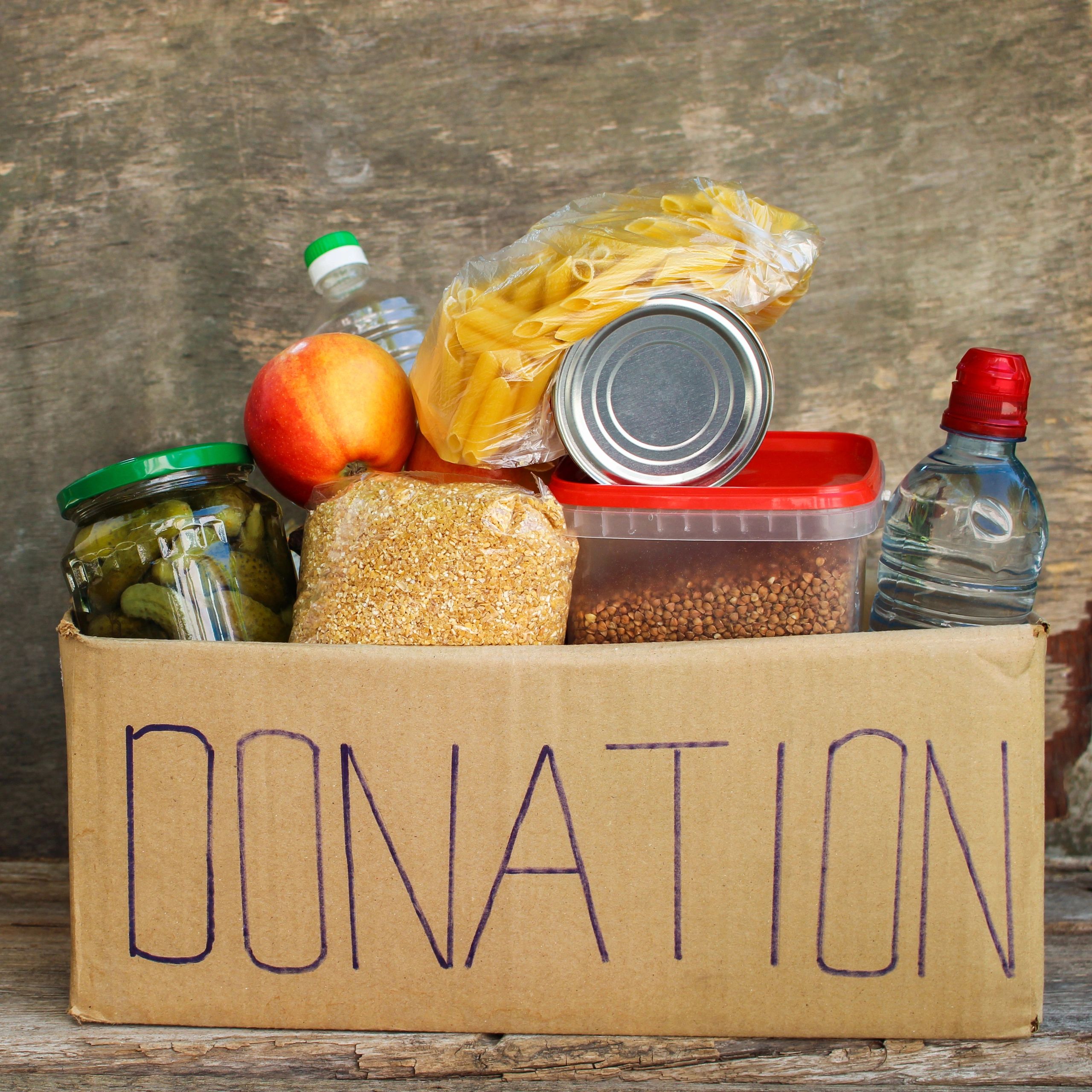 Box filled with food donations including apples, pasta, and water.