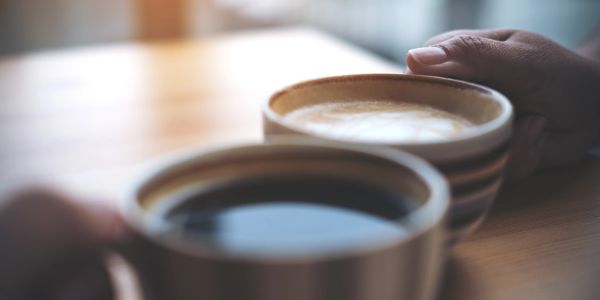Two cups of coffee held by hands on a wooden table.