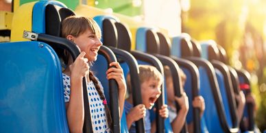 Kids excitedly wait on a blue amusement park ride under bright sunlight.